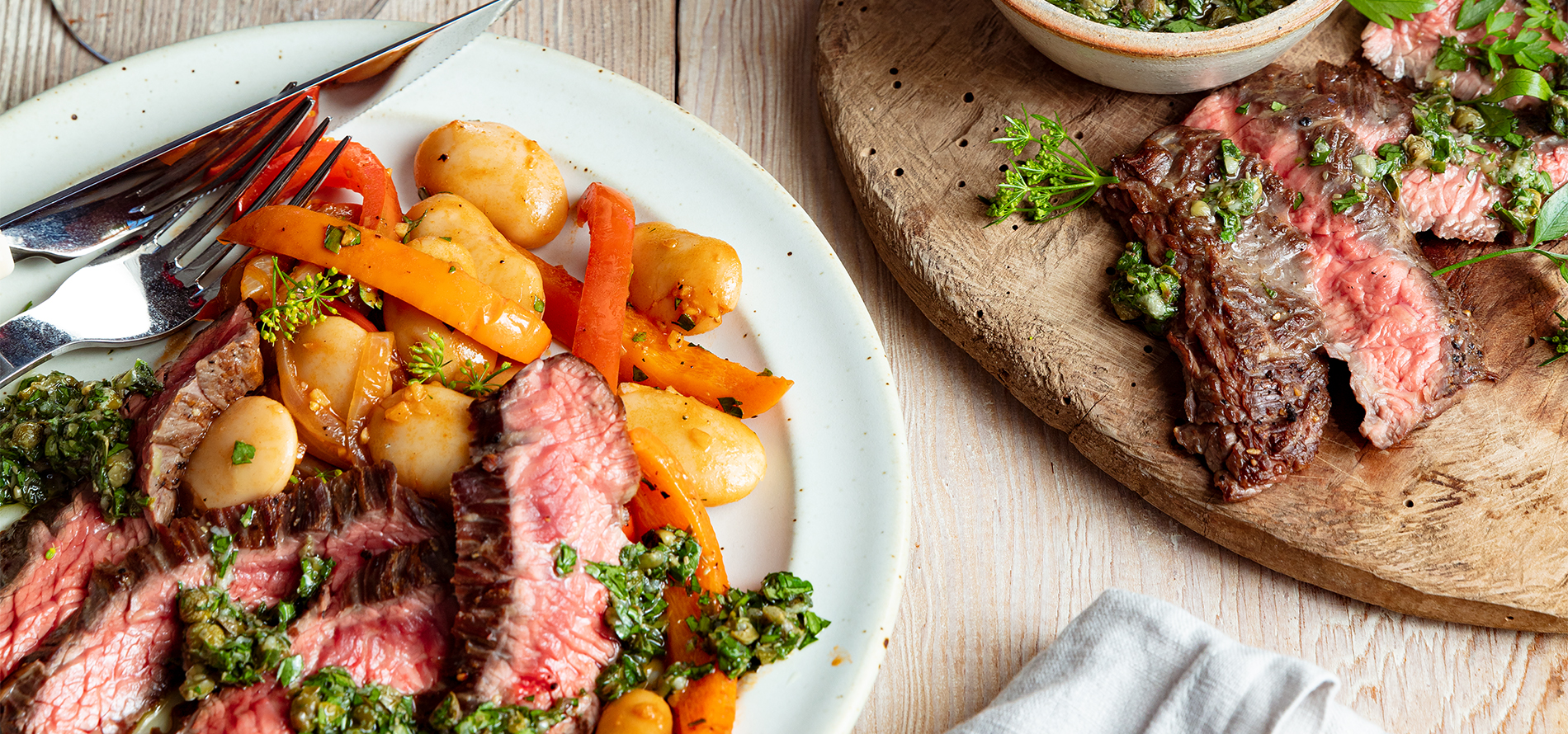 Plate of Bistro Steak with herbs and utensils on a wood table