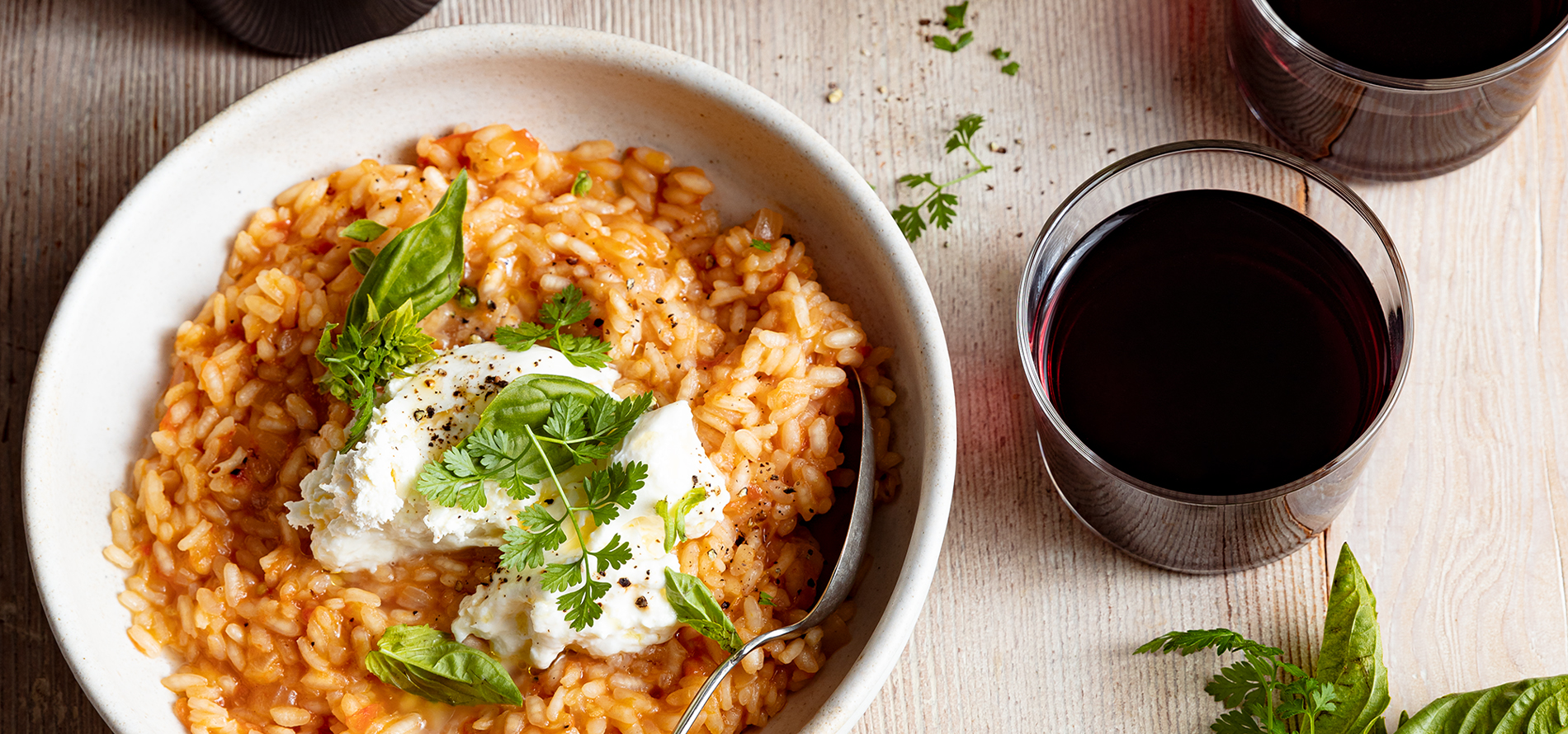 Tomato Risotto in a white bowl on a wood table with glasses of red wine beside