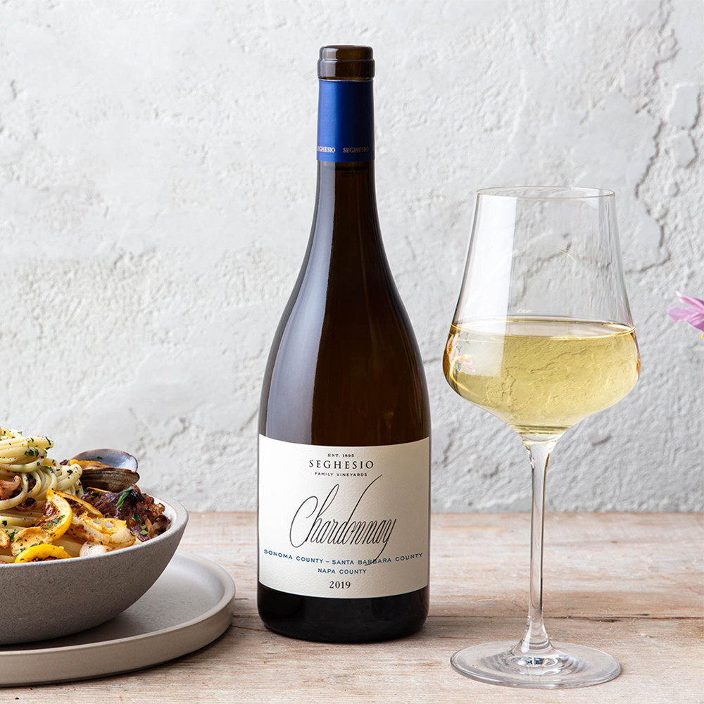 Seghesio Chardonnay wine bottle on wood table with a glass of white wine and seafood pasta