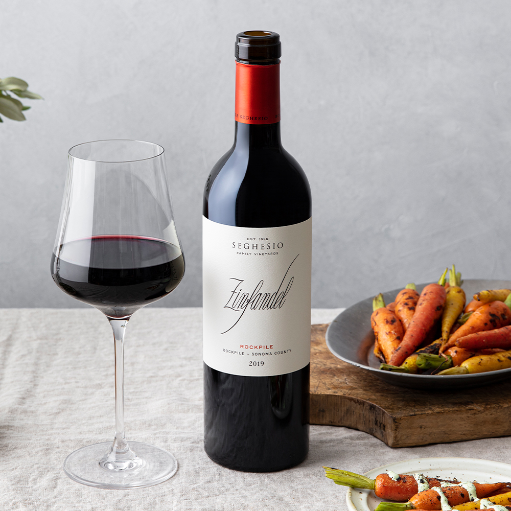 Rockpile Zinfandel bottle on table with a glass of red wine and small, roasted carrots